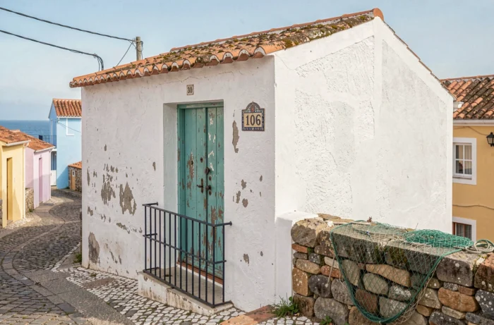 Façade authentique d'une maison de pêcheur portugaise avec porte turquoise et vue sur la mer en arrière-plan